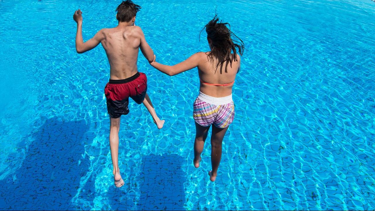 Ein Junge und ein Mädchen springen gemeinsam in ein Schwimm-Becken.