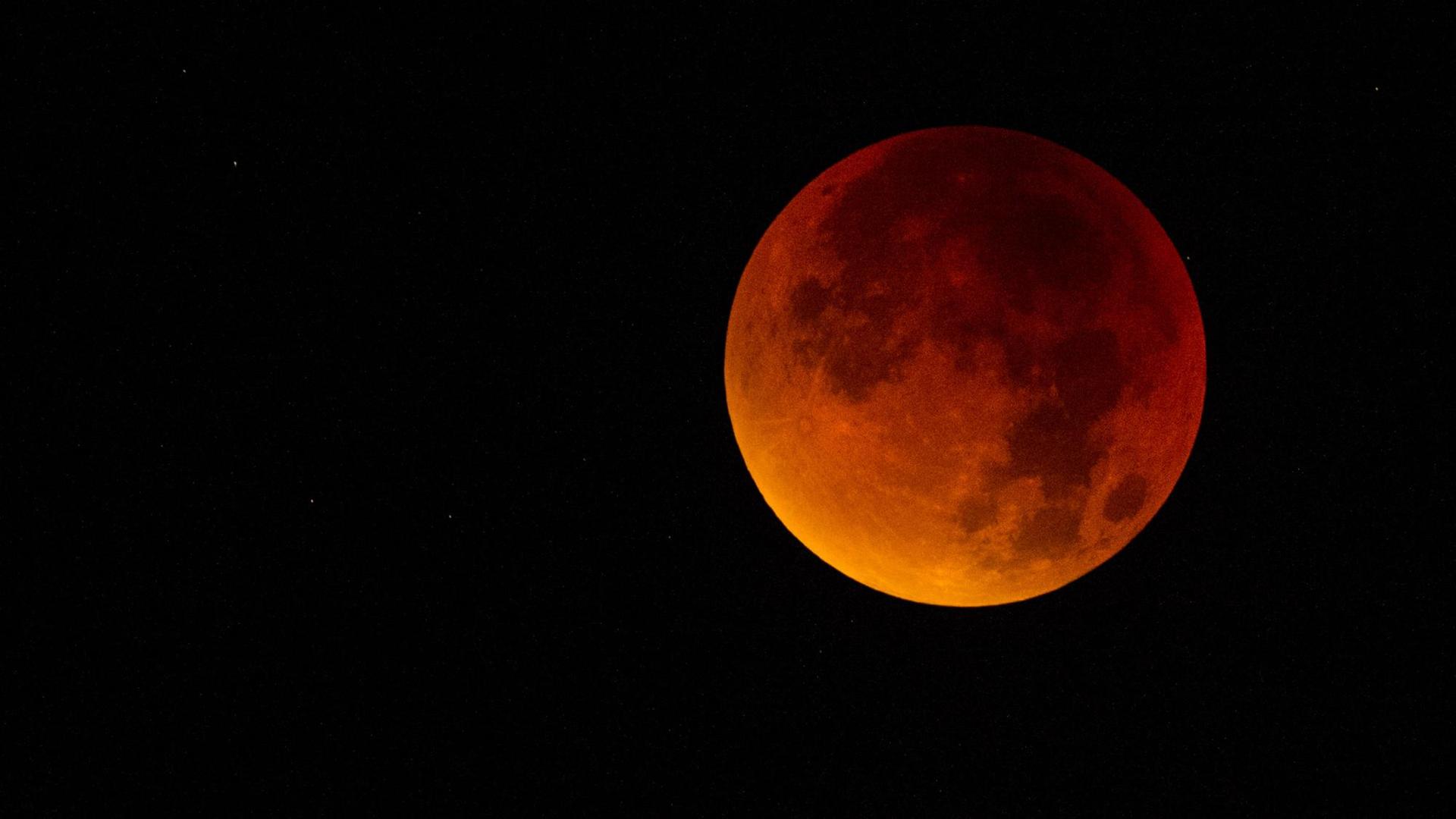 Der Mond erscheint tief-rot gefärbt. Der Himmel ist nacht-schwarz.