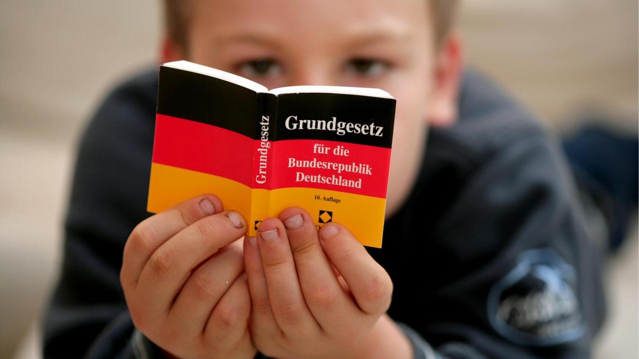 Ein Kind liest in einem Mini-Grundgesetz. 