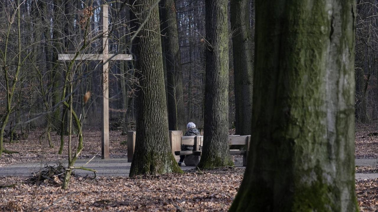 Ein Waldfriedhof in Herten im Ruhrgebiet. Auf einer Bank sitzt eine Frau, davor steht ein Holzkreuz.