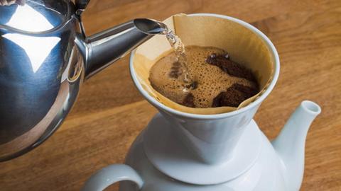 In einen Porzellan-Filter mit Filtertüte wird zum brühen von Kaffee heißes Wasser geschüttet.