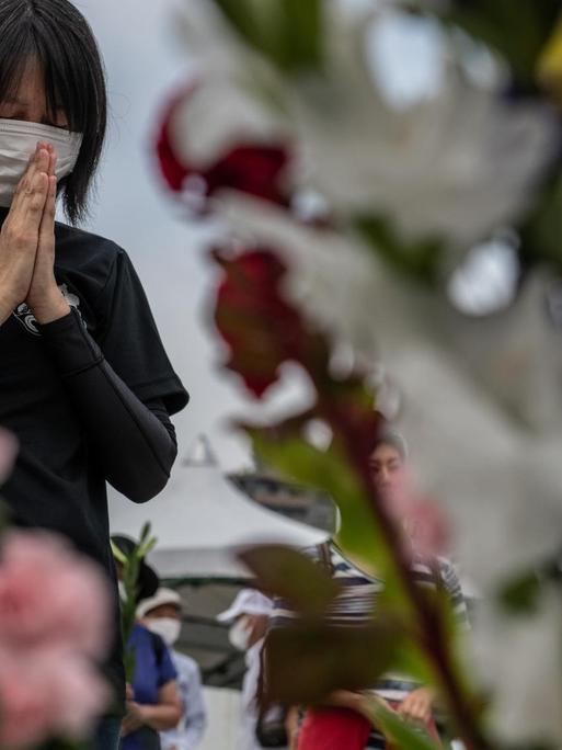 Eine Frau mit Mundschutz betet zwischen Blumen