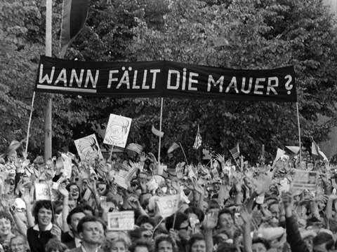 Während des Kennedy-Besuchs in West-Berlin 1963: Menschen halten ein Transparent mit der Frage "Wann fällt in Mauer?" in die Höhe.