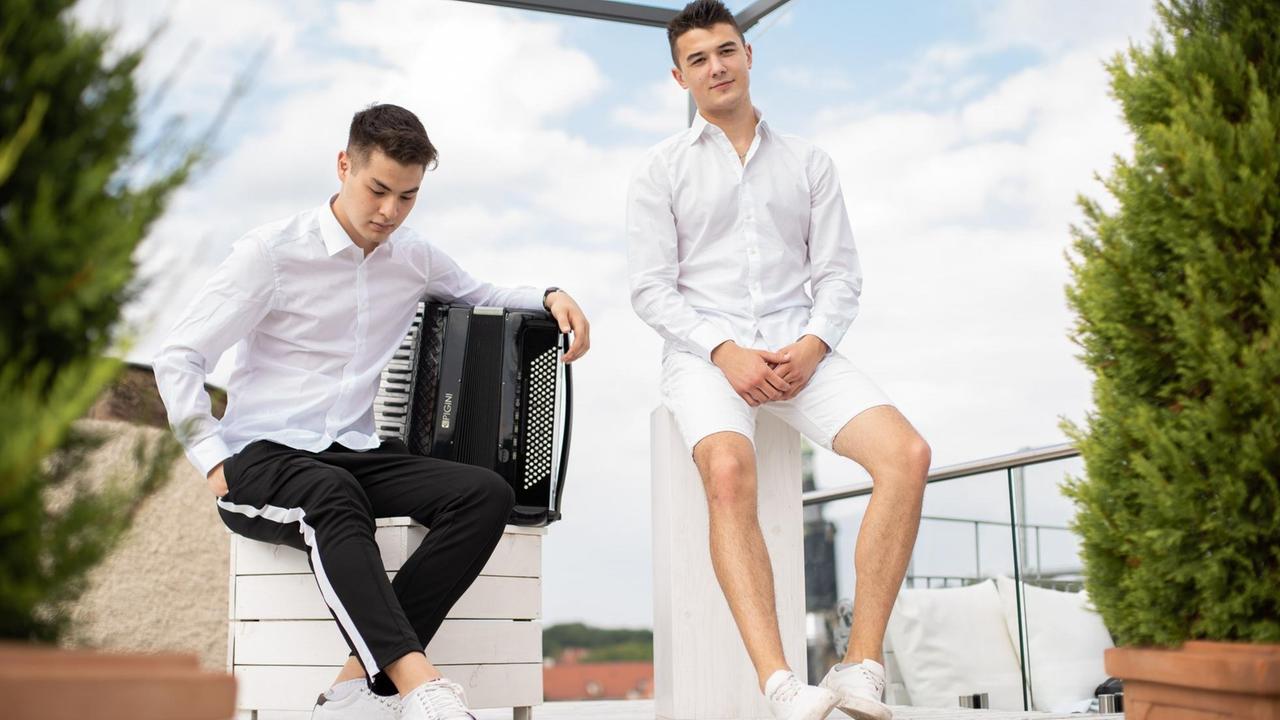 Beide Akkordeonisten sitzen in sommerlicher Kleidung auf einer Dachterasse, hinter ihnen blauer Himmel