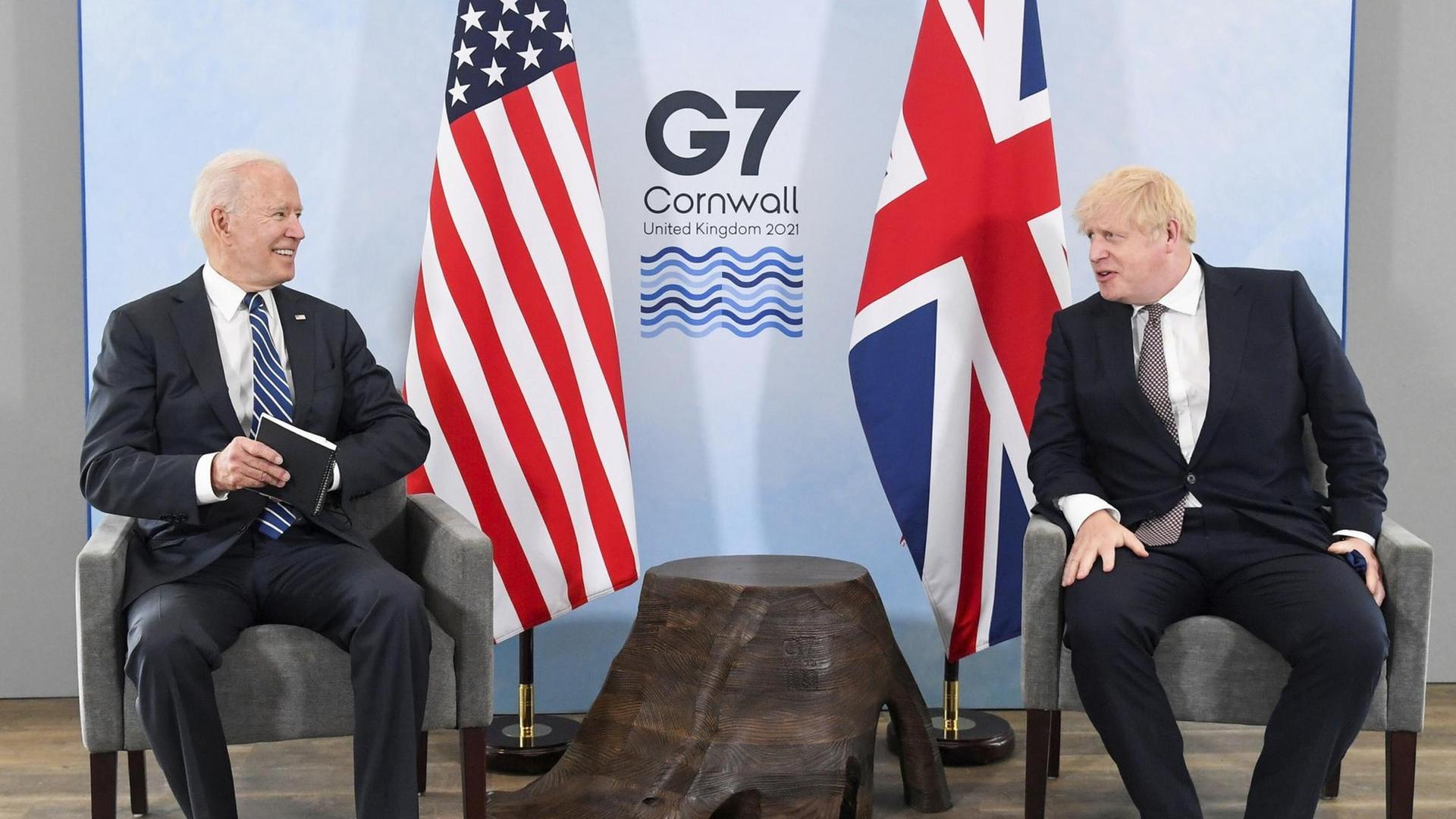 Joe Biden und Boris Johnson sitzen auf zwei Sesseln im Hintergrund das Logo des G7-Gipfels und die Flaggen der USA und Großbritanniens.