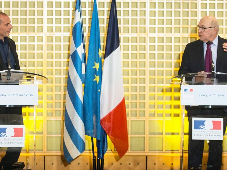 Yannis Varoufakis und Michel Sapin sprechen an Stehpulten bei einer Pressekonferenz, zwischen ihnen die Flaggen beider Länder und die der EU.