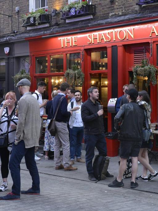 Sie sehen einen Pub in London von außen, viele Menschen stehen davor.