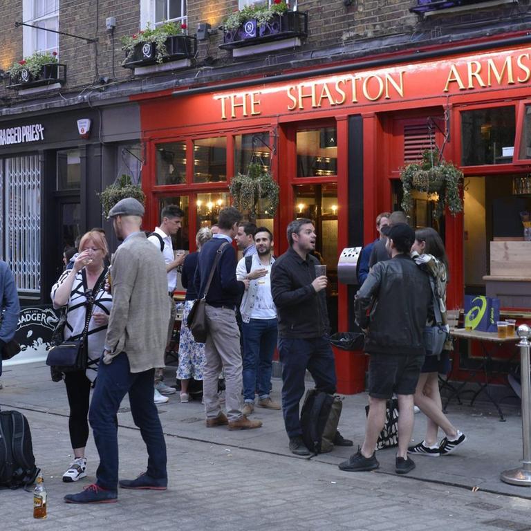 Sie sehen einen Pub in London von außen, viele Menschen stehen davor.