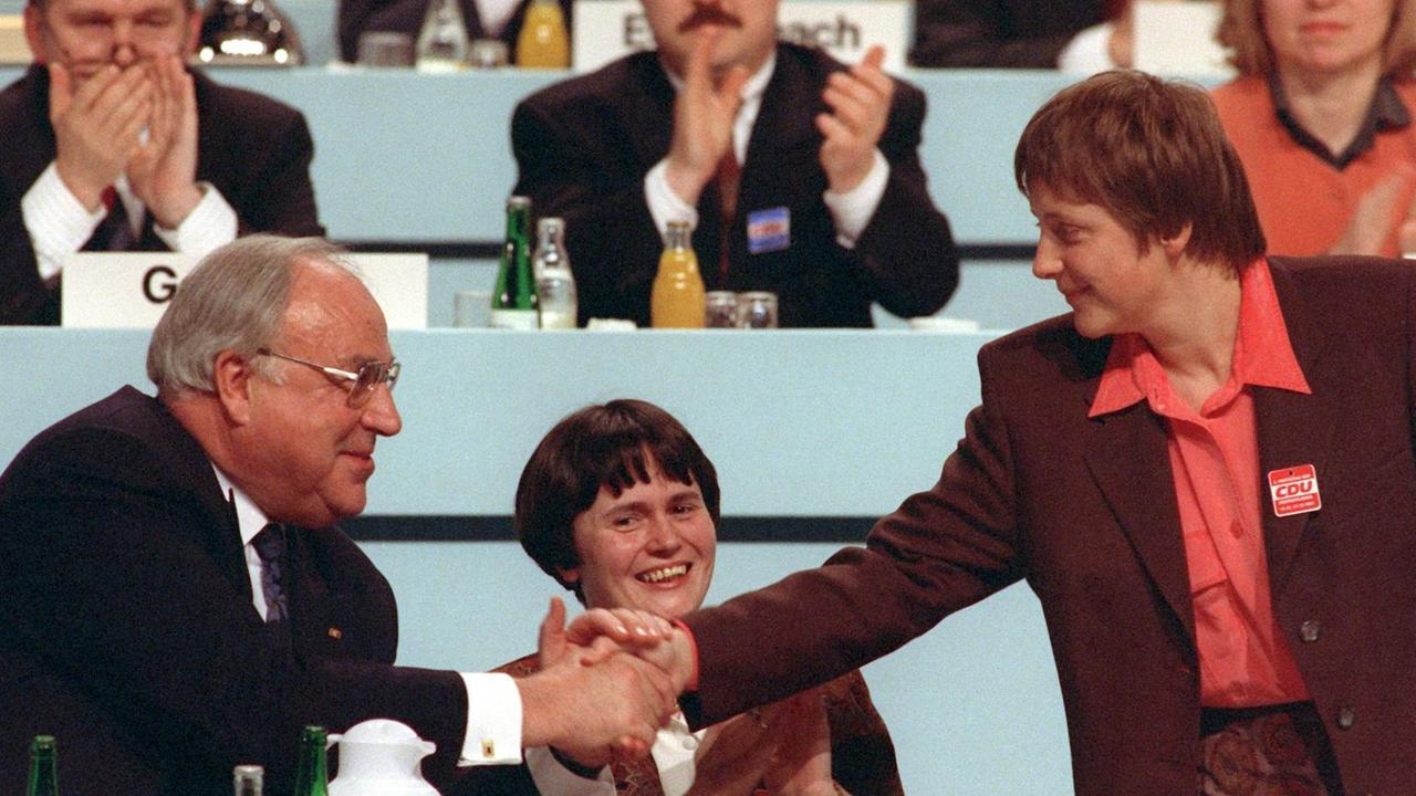 Christine Lieberknecht (Mitte) neben dem damaligen Bundeskanzler Helmut Kohl, der seiner neugewählten Stellvertreterin, der damaligen Frauenministerin Angela Merkel während des Parteitags der CDU am 15. Dezember 1991 im Kulturpalast in Dresden per Handschlag gratuliert. 