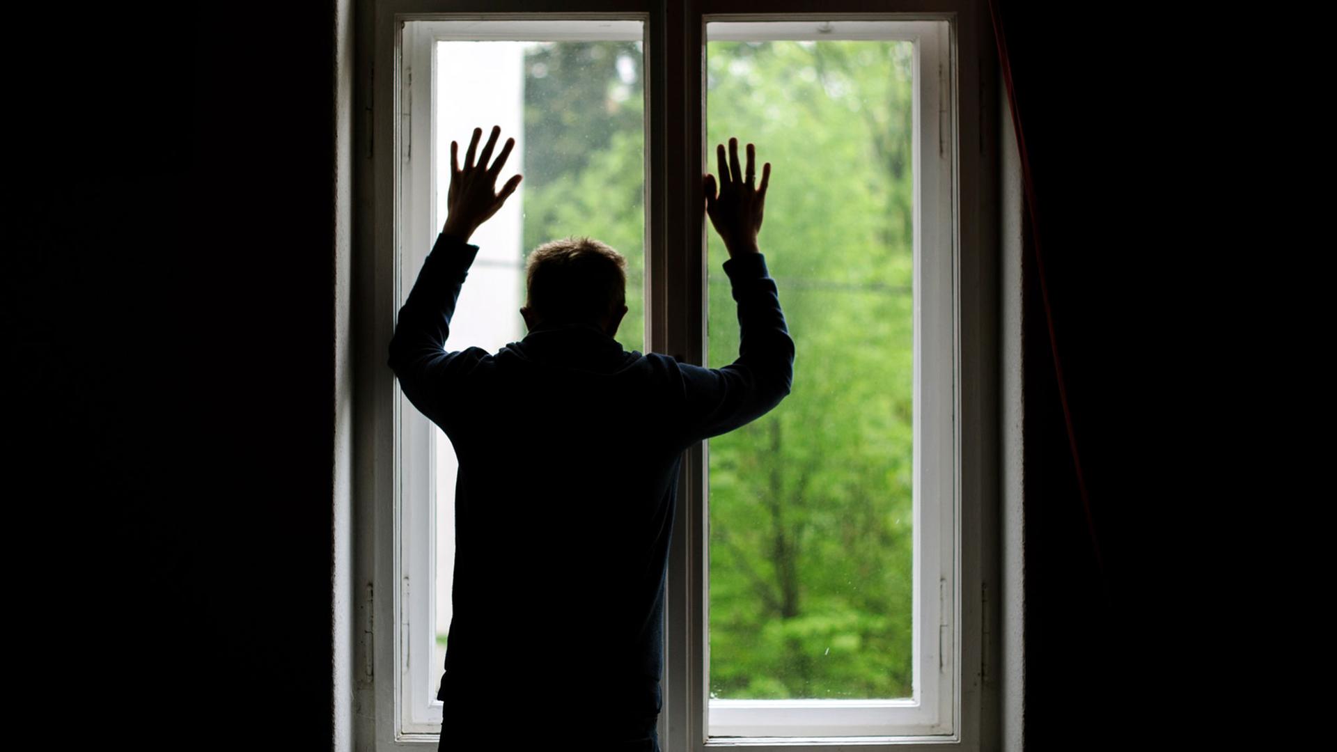 Ein Mann steht allein an einem Fenster und schaut nach draußen