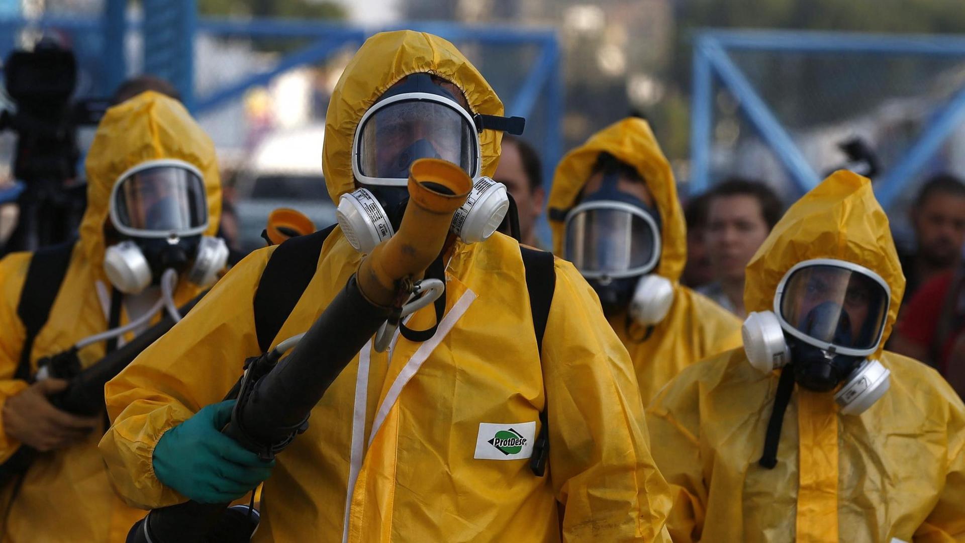 Einsatzkräfte in gelben Schutzanzügen mit Geräten für die Desinfektion.