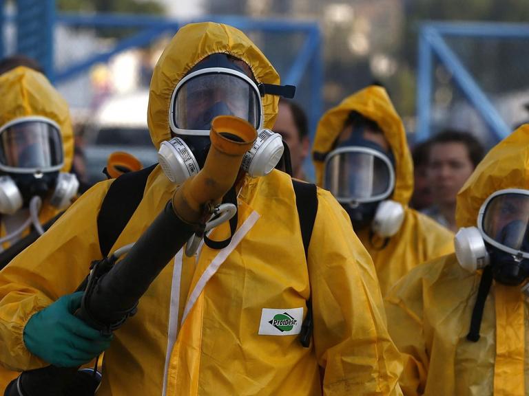 Einsatzkräfte in gelben Schutzanzügen mit Geräten für die Desinfektion.