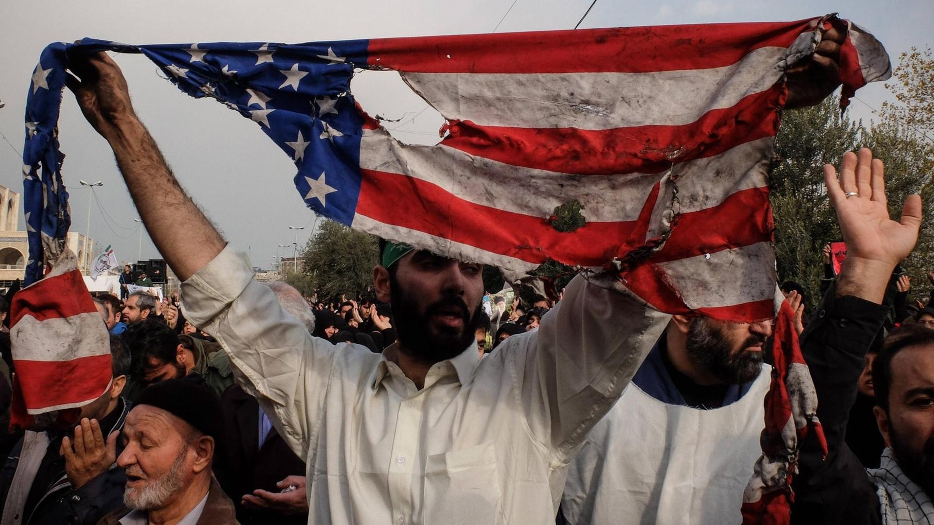 Ein Mann hält bei Protesten in der iranischen Hauptstadt Tehran eine verannte Fahne der USA hoch.