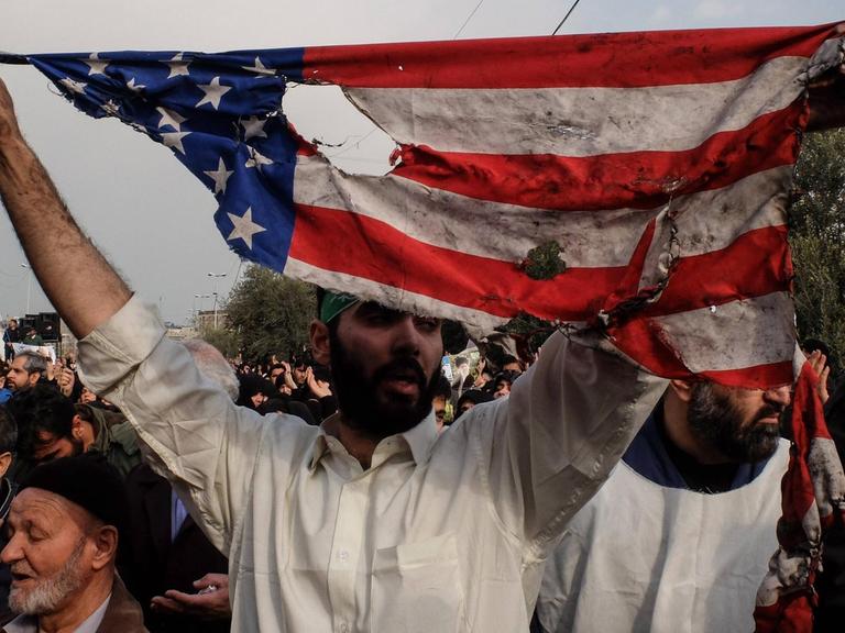 Ein Mann hält bei Protesten in der iranischen Hauptstadt Tehran eine verannte Fahne der USA hoch.