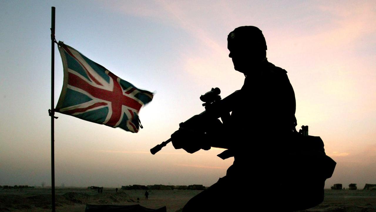 Ein bewaffneter britischer Soldat kniet im Gegenlicht in der Wüste. Hinter ihm ist die britische Flagge zu sehen.