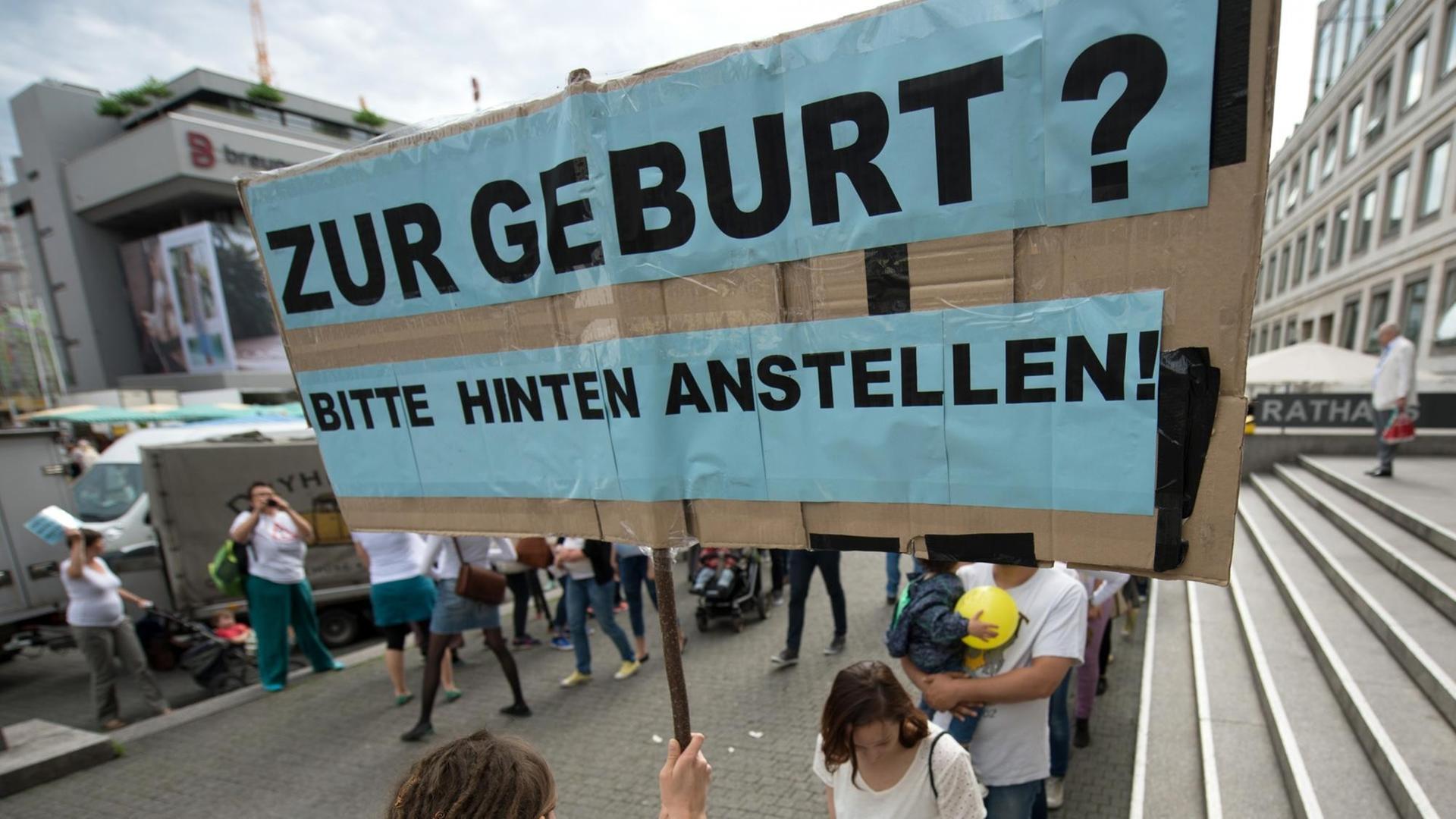 Eine Hebamme hält in Stuttgart (Baden-Württemberg) ein Schild hoch mit der Aufschrift "Zur Geburt? Bitte hinten anstellen!" Rund 50 Hebammen protestierten mit einem Flashmob für bessere Arbeitsbedingungen.