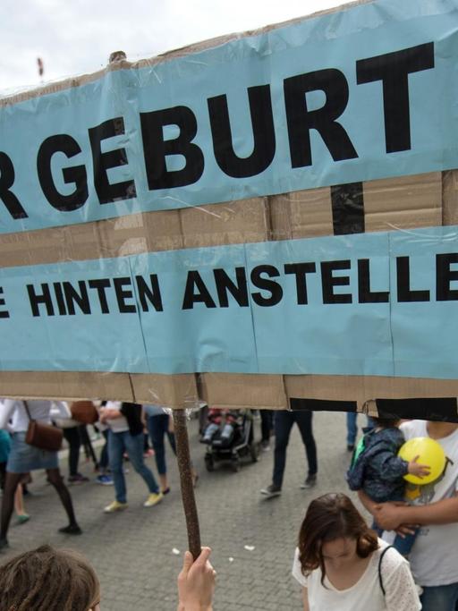 Eine Hebamme hält in Stuttgart (Baden-Württemberg) ein Schild hoch mit der Aufschrift "Zur Geburt? Bitte hinten anstellen!" Rund 50 Hebammen protestierten mit einem Flashmob für bessere Arbeitsbedingungen.