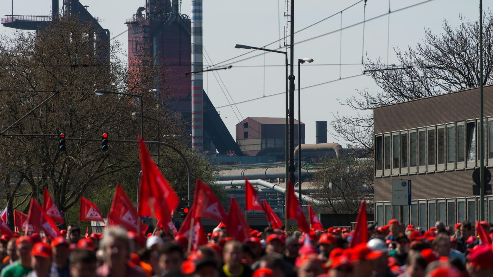 Demonstranten mit Fahnen und Transparenten gehen am 11.04.2016 in Duisburg (Nordrhein-Westfalen) zum Kundgebungsort. Bei einem bundesweiten Aktionstag wollen tausende Stahlkocher für ihre Arbeitsplätze auf die Straße gehen.