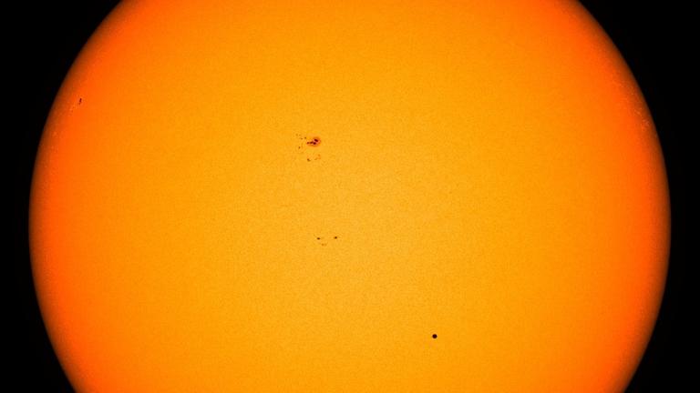 Merkur erscheint beim Transit vor der Sonne als kleiner schwarzer Punkt – weiter oben sind einige Sonnenflecken zu erkennen
