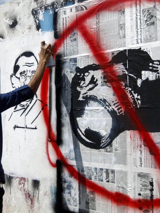 Ein Mann sprayt ein Bild von einer rot durchgestrichenen Kamera an eine Mauer