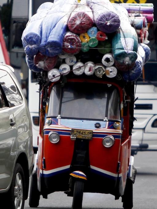 Ein überladenes Taxi, Bajaj genannt, zwischen Autos, Bussen und Mopedfahrern in Jakarta