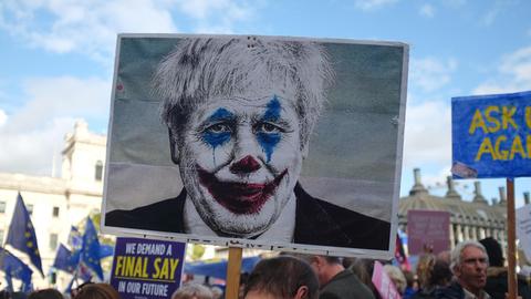 person holding sign with picture of a man wearing clown face art