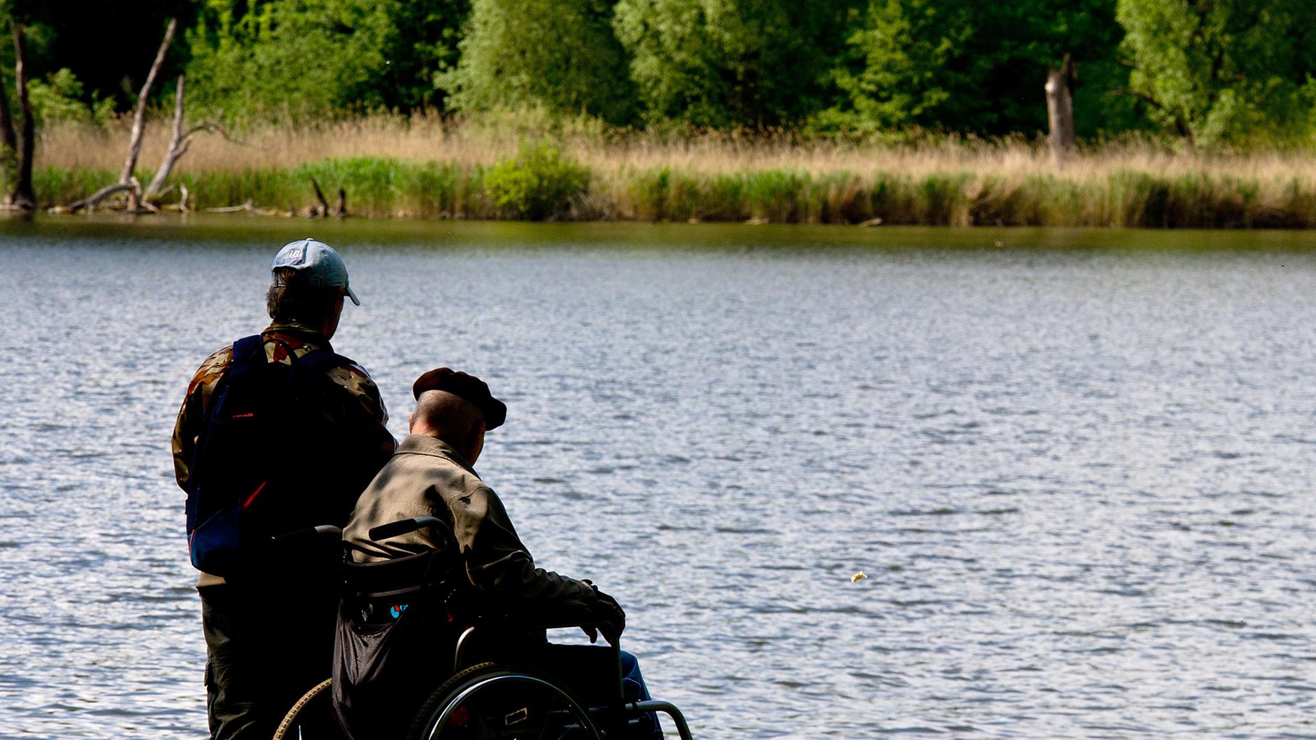 Ein Mann begleitet am 07.05.2014 einen älteren Herren in einem Rollstuhl um den Malchower See in Berlin.