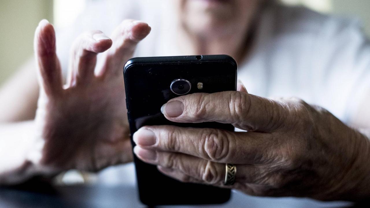 Eine Seniorin hält ein Smartphone in der Hand.