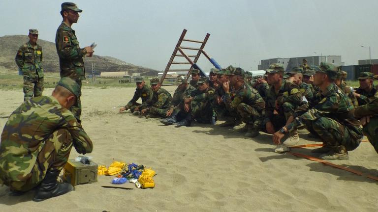 Afghanische Soldaten hocken vor Plastikspielzeug im Sand.