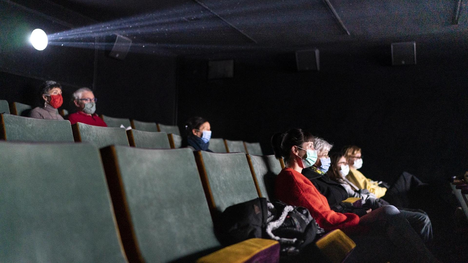 Mehrere Menschen sitzen mit Abstand und Maske in einem Kino.