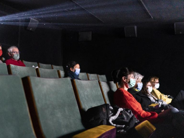 Personen sitzen mit Abstand und Maske in einem Kino.