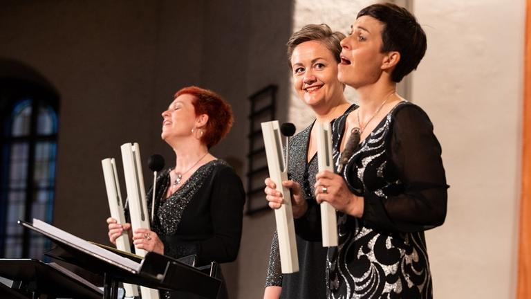 Die Sängerinnen vom Trio Mediaeval in schwarzer Konzertkleidung bei ihrem Konzert in Leipzig, in der Hand haben Sie Glockenstäbe
