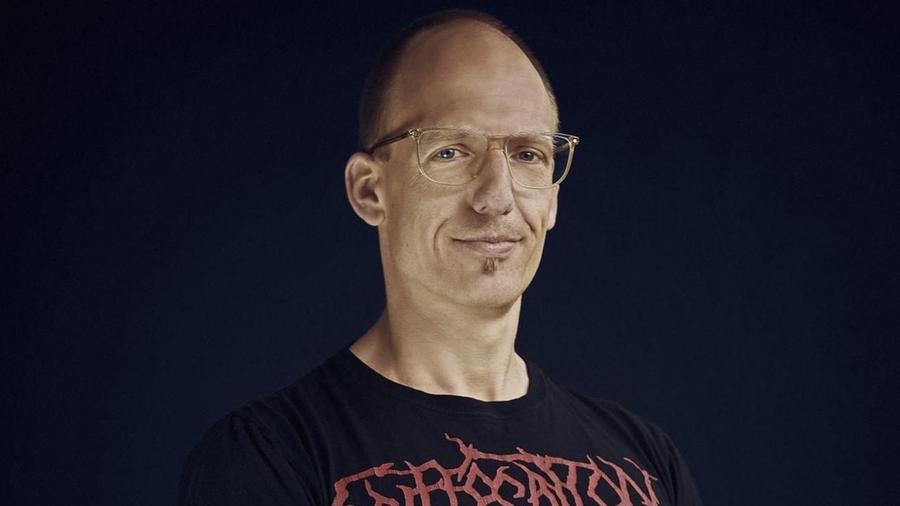 Jörg Scheller trägt eine Brille und ein schwarzes T-Shirt mit dem Namensschriftzug einer Heavy Metal Band