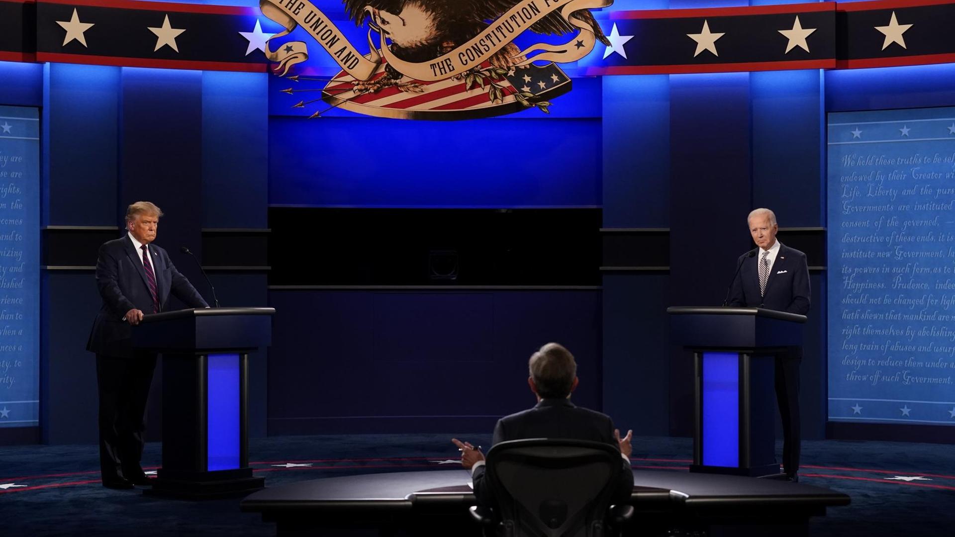 Donald Trump (l.) und Joe Biden stehen während des ersten TV-Duells vor der Präsidentschaftswahl 2020 auf einer Bühne an Redepulten. Im Vordergrund ist der Moderator der Debatte, Chris Wallace, von hinten zu sehen. Donald Trump (l.) und Joe Biden stehen während des ersten TV-Duells vor der Präsidentschaftswahl 2020 auf einer Bühne an Redepulten. Im Vordergrund ist der Moderator der Debatte, Chris Wallace, von hinten zu sehen.