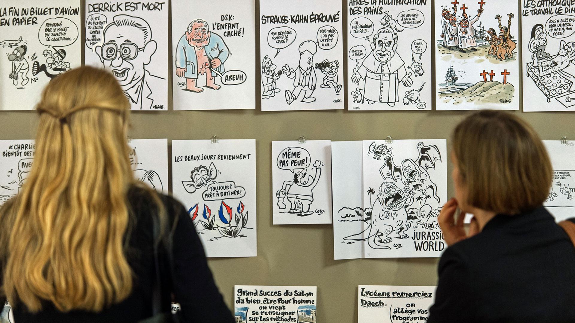 Besucherinnen der Ausstellung "Caricatures" betrachten Karikaturen von Künstlern der Zeitschrift "Charlie Hebdo".