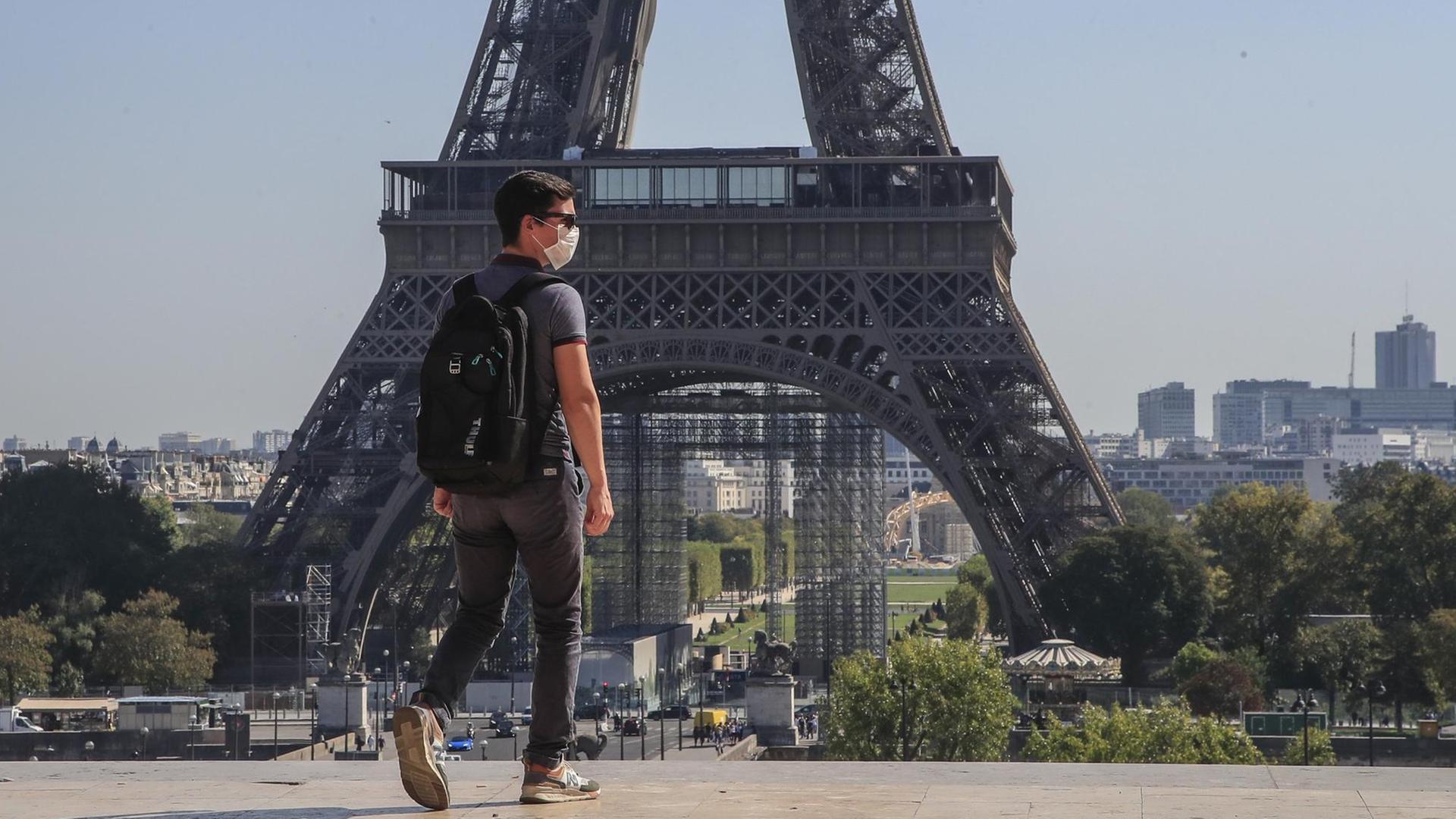 Ein Passant geht mit Mundschutzmaske über den Place du Trocadéro, während im Hintergrund ein Teil des Eiffelturms zu sehen ist.