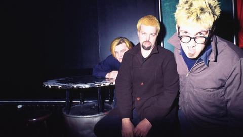 Die Musiker der Band Eels albern in typischen 90s-Klamotten vor der Kamera herum.