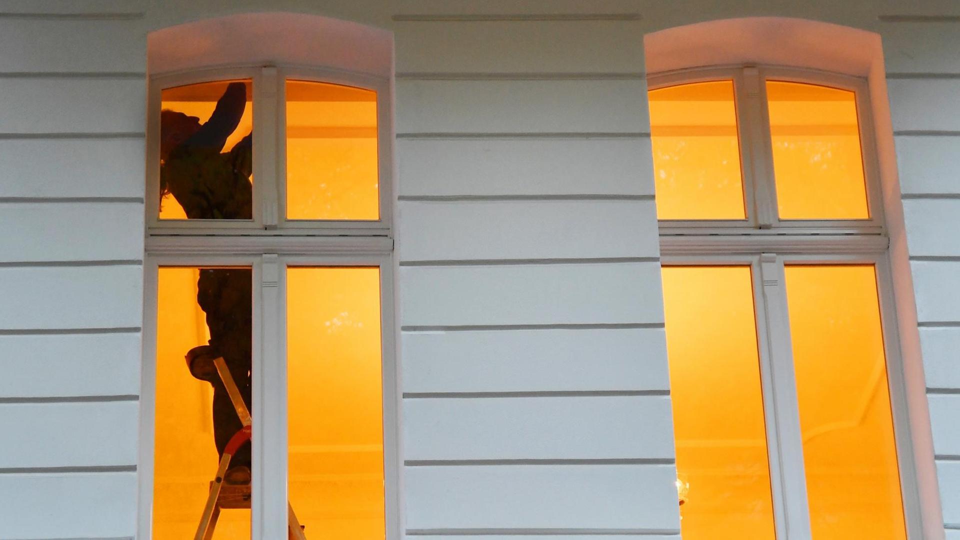 Ein Mann steht in Berlin an einem Fenster in einer Wohnung auf einer Leiter.