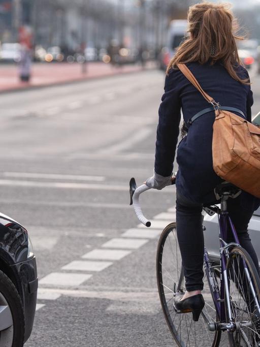Berlin: Eine Fahrradfahrerin fährt auf einem Fahrradweg auf einer Kreuzung zwischen zwei Autos entlang.