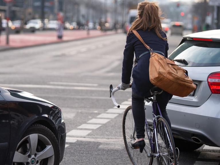 Berlin: Eine Fahrradfahrerin fährt auf einem Fahrradweg auf einer Kreuzung zwischen zwei Autos entlang.