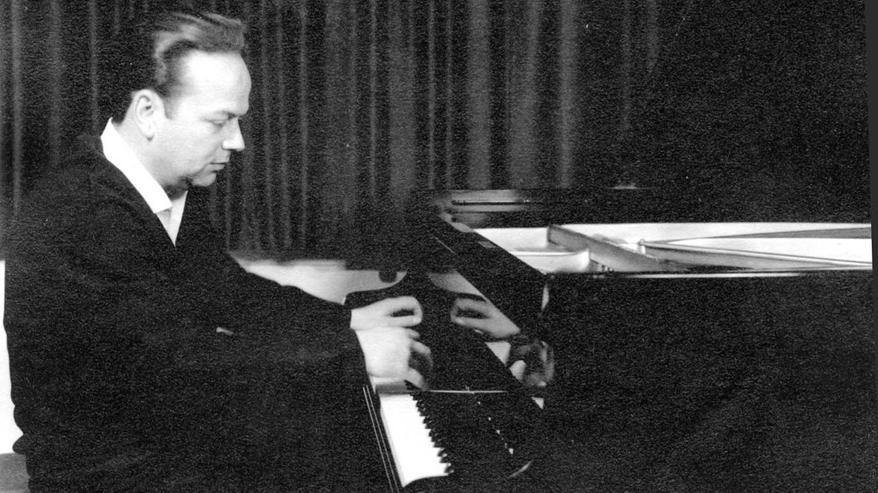 Schwarz-weiß Foto des Pianisten Werner Haas. Er sitzt an einem schwarzen Flügel und spielt, er schaut auf die Tasten, er trägt ein weißes Hemd und darüber einen dunklen Pullover, die Haare sind zurückgekämmt.
