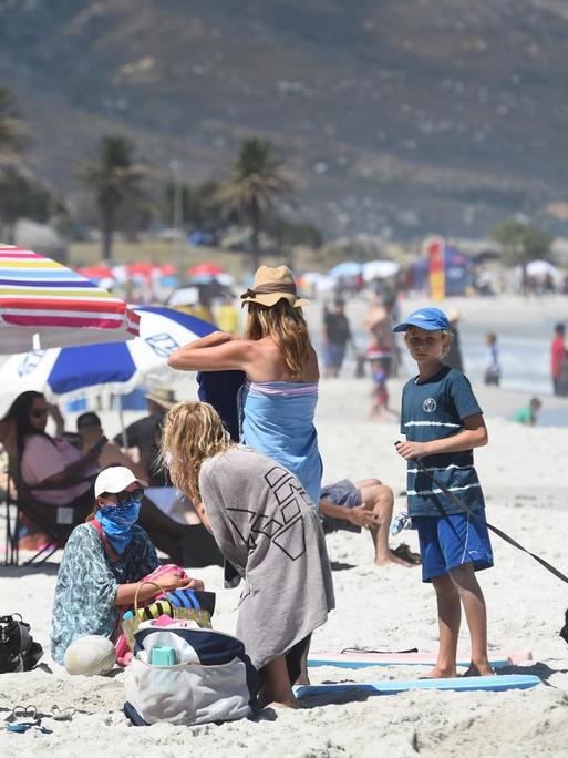 Blick auf den Strand in Kapstadt, Menschen tragen Masken und verbringen Zeit an Land und im Wasser