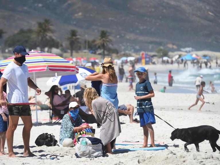 Blick auf den Strand in Kapstadt, Menschen tragen Masken und verbringen Zeit an Land und im Wasser