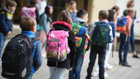 Schülerinnen und Schüler einer Grundschule stehen mit Abstand zueinander auf dem Schulhof