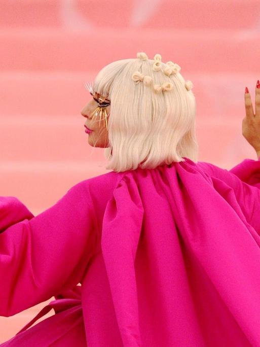 Profil der Musikerin Lady Gaga mit seitlich erhobenen Händen, in einer wallenden pinken Robe