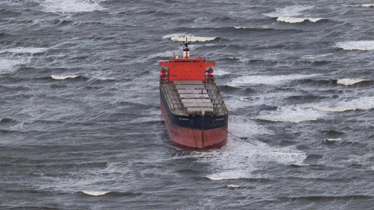 Foto aus dem Hubschrauber auf das rot-schwarze Schiff, das in aufgewühlter See festsitzt und Anker geworfen hat.