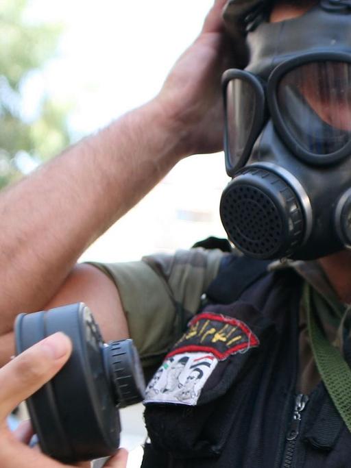 Ein syrischer Soldat hat eine Gasmaske auf, eine Hand reicht ihm einen neuen Filter.