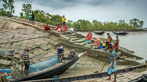 An einem indischen Flussufer sind buntgekleidete Menschen mit ihren Booten zu sehen.
