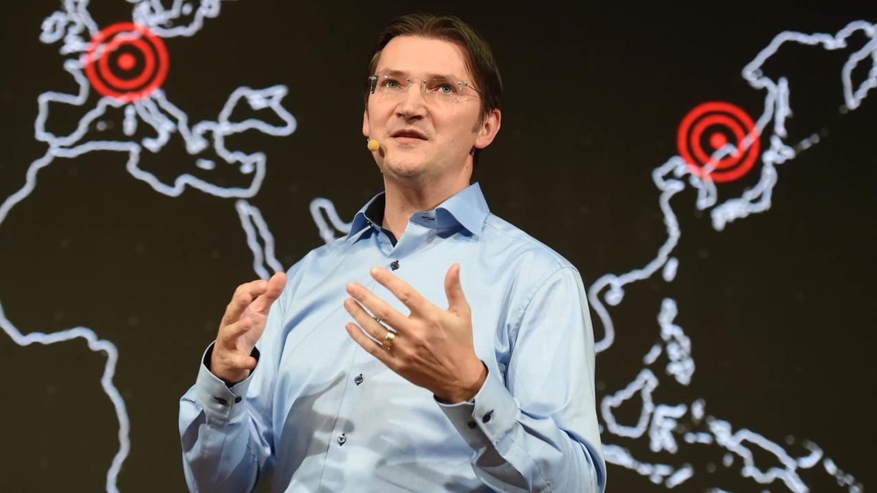 Johann Jungwirth bei einem Vortrag, im Hintergrund eine stilisierte Weltkarte
