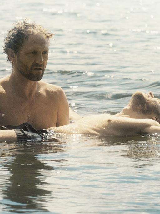 Filmszene aus "Im Namen des..." von Małgorzata Szumowska. Andrzej Chyra als Pater Adam (l) hält Mateusz Kosciukiewicz als Lukasz im Wasser in seinen Armen.